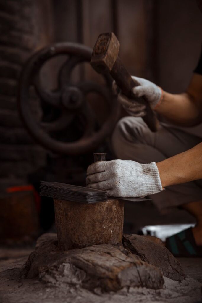 Skilled worker using a hammer to shape metal in a traditional workshop setting.