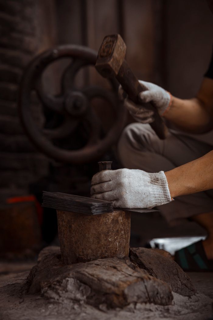 Skilled worker using a hammer to shape metal in a traditional workshop setting.