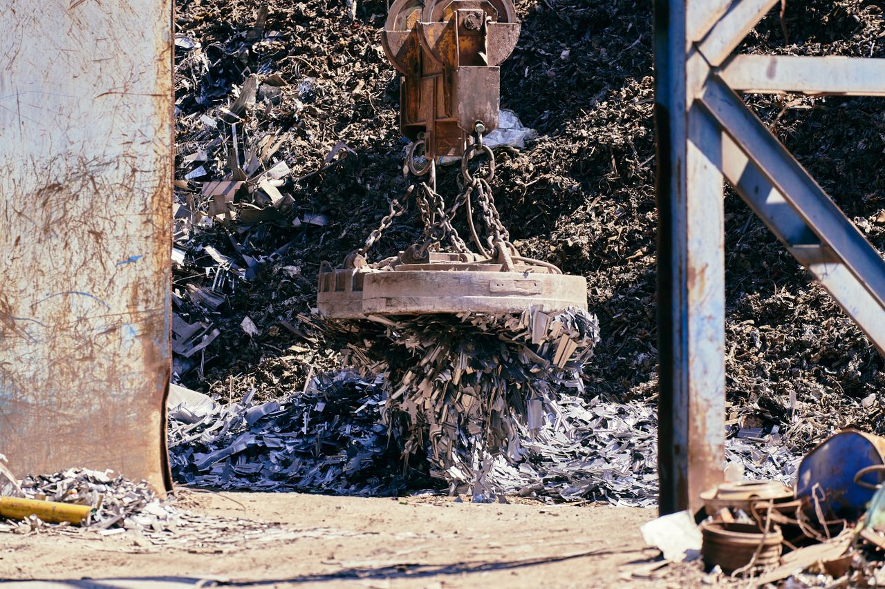 Magnet crane lifting scrap metal in a recycling yard.
